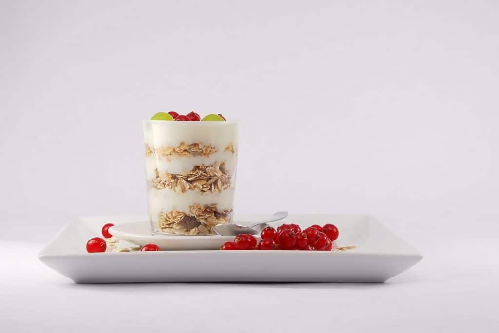 Un yaourt avec du granola et des baies sur une assiette blanche.