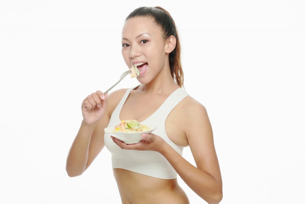 Une femme mangeant un bol de salade avec de l'acide linoléique conjugué sur un fond blanc.