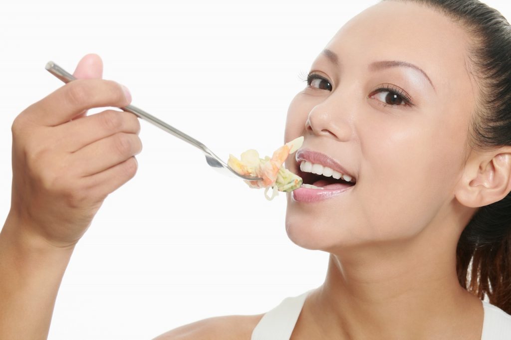 Une femme qui consomme des aliments riches en probiotiques avec une fourchette sur un fond blanc.