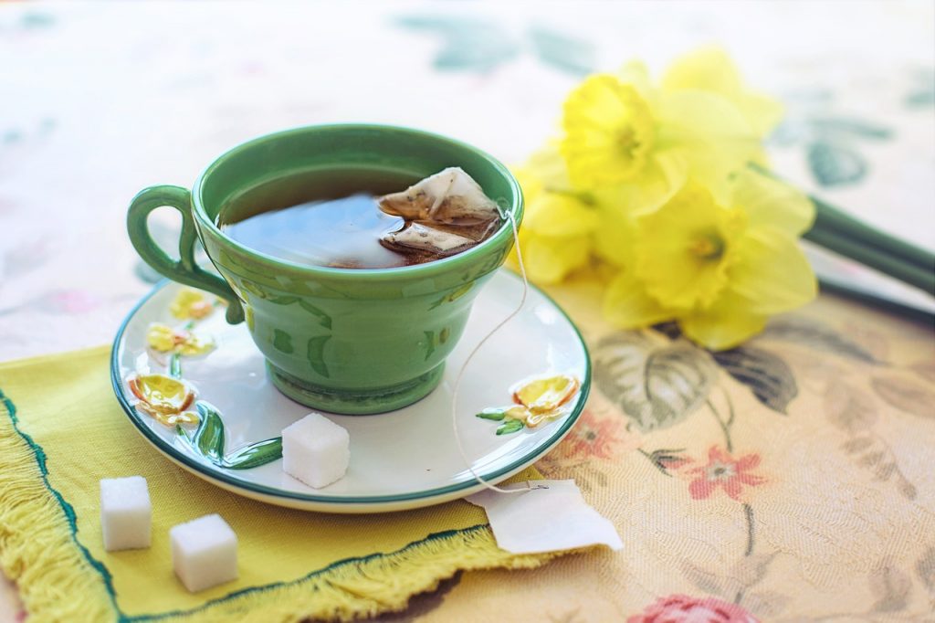 Una tazza di tè orthosiphon con zollette di zucchero e narcisi.