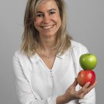 Una donna con tre mele davanti a uno sfondo grigio.