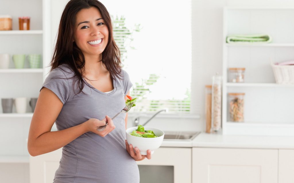 Una donna incinta che tiene una ciotola di insalata in cucina.