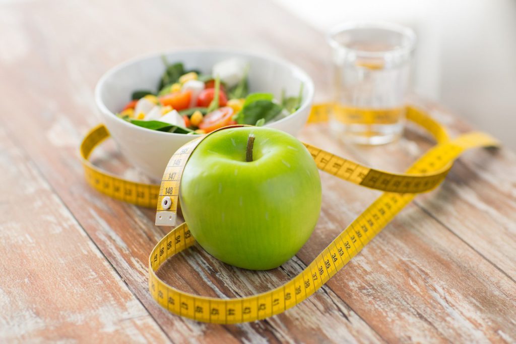 Una mela verde accanto a un metro a nastro e una ciotola di insalata.