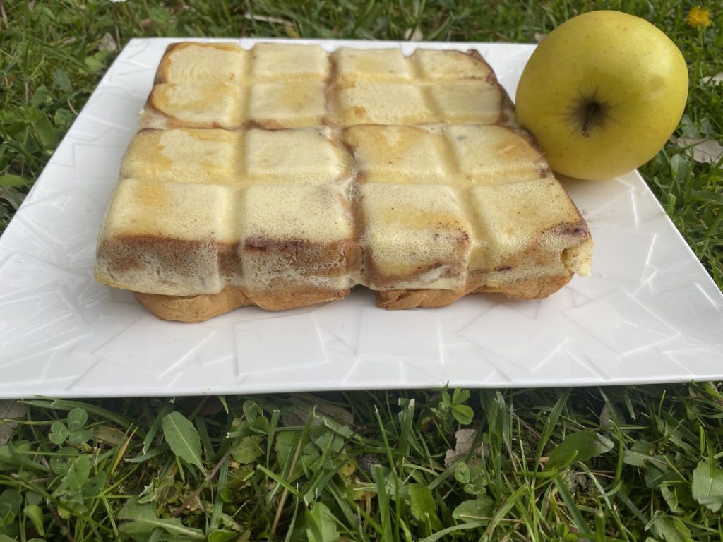 Un pezzo di pane quadrato su un piatto con accanto una mela.