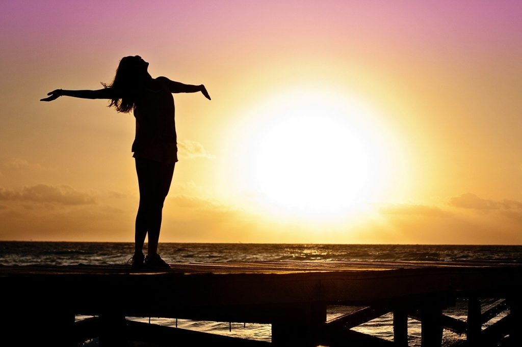 Una silhouette di una donna in piedi su un molo al tramonto.